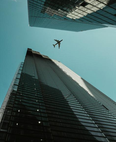 A ground view of a plane flying high above skyscrapers