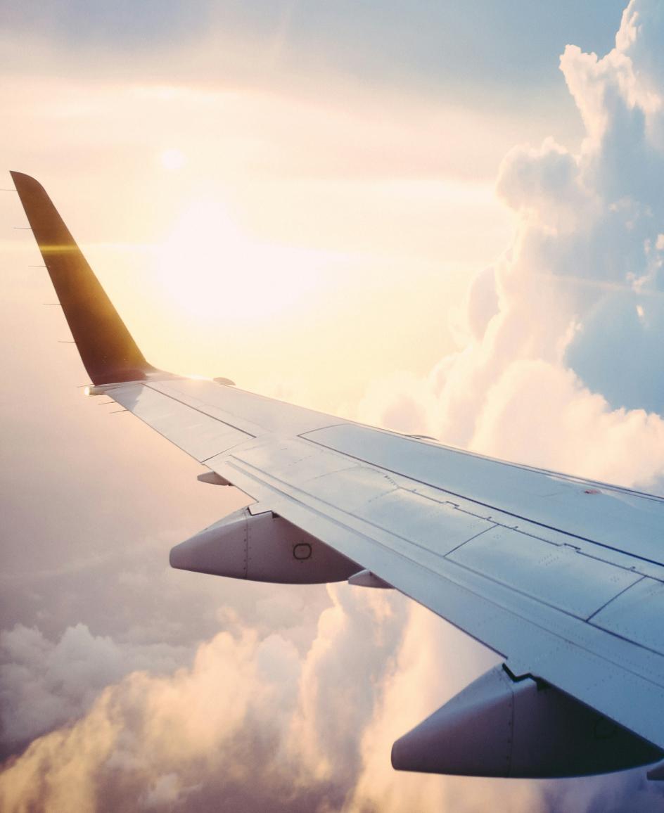 A picture of a plane wing in clouds and sunshine taken from a passenger window